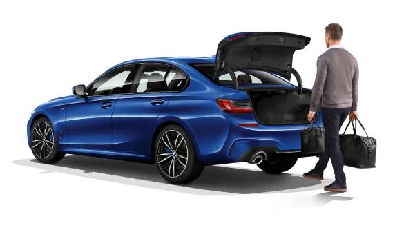 BMW 3 Series Sedan, automatic tailgate operation Three-quarter rear shot of standing BMW 3 Series Sedan with driver automatically opening the tailgate with his foot.