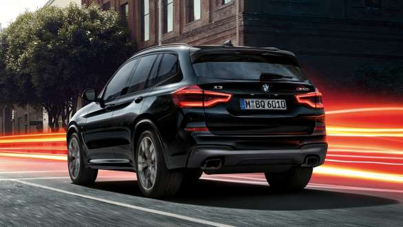 BMW X3 M40i, three-quarter rear view. BMW X3 M40i in Black Sapphire metallic, driving, exterior, three-quarter rear view before an urban background with light strips.