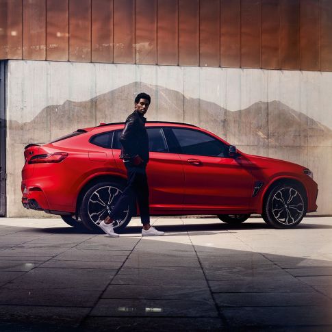 BMW X4 M Competition, side view with young man. BMW X4 M Competition in Toronto Red metallic, exterior, side view with young man.