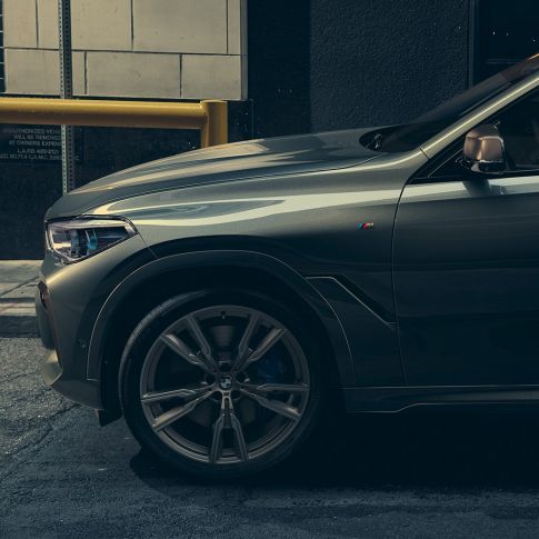 BMW X6 M50i SUV in lateral perspective Man leaning on BMW X6 M50i SUV in lateral perspective in front of an urban setting