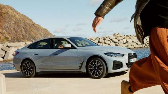 BMW Service Inclusive for new cars BMW Service Inclusive woman walks in front of BMW i4 at the coast