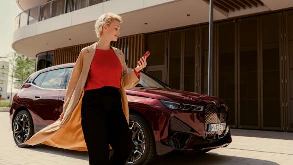 Application My BMW Application My BMW, femme dans la rue avec un smartphone à la main et un véhicule BMW en arrière-plan