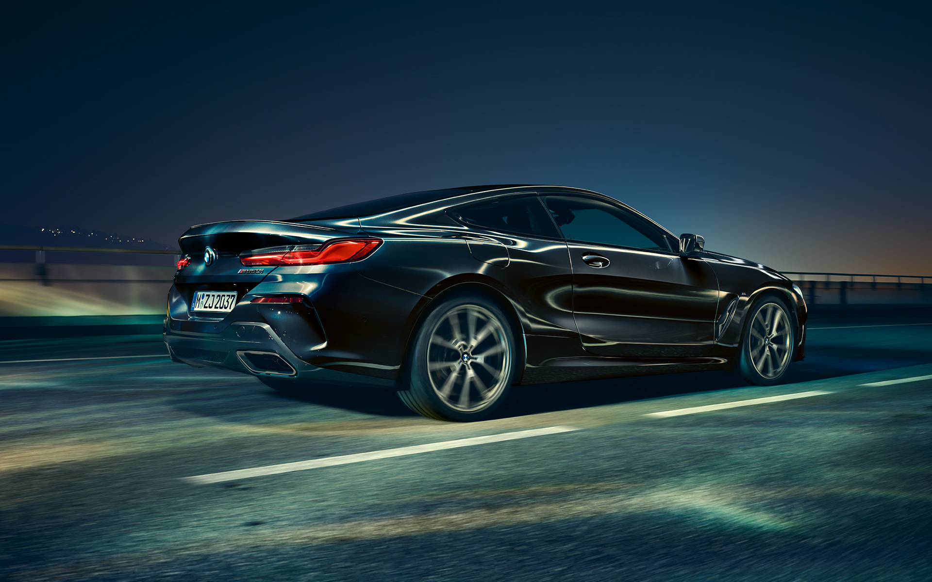 A three-quarter rear driving shot of the BMW 8 Series Coupé in an urban setting at night.