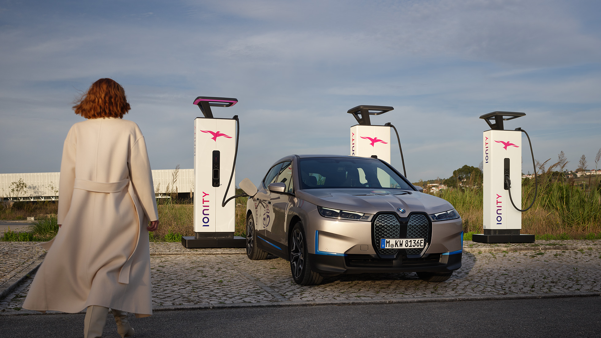 BMW iX vue de trois quarts avant à une borne de recharge BMW iX Kaschmirsilber i20 vue de trois quarts avant à une borne de recharge