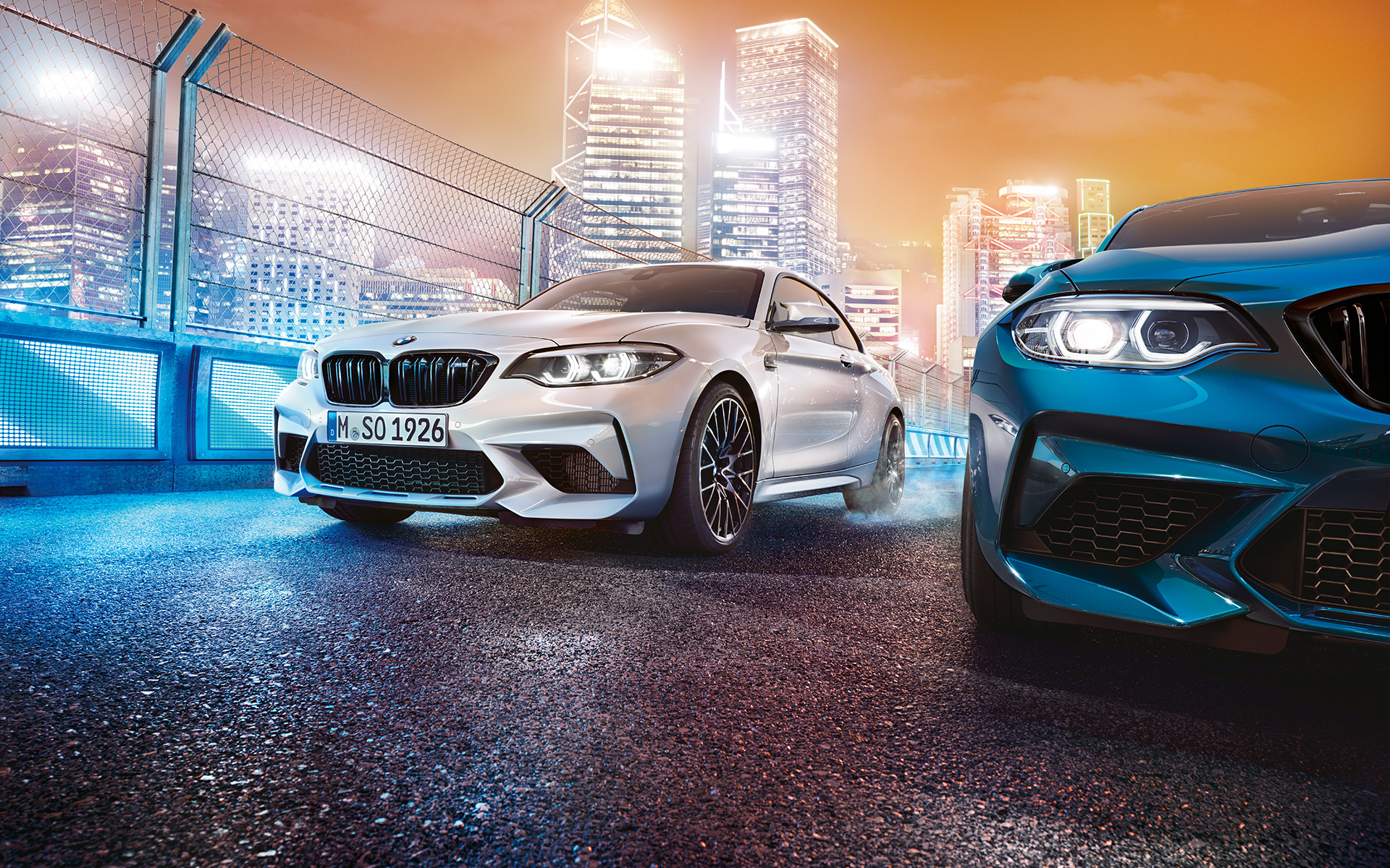 White and blue BMW M2 Competition in front view standing in front of nocturnal cityscape. White and blue BMW M2 Competition in front view standing in front of nocturnal cityscape.