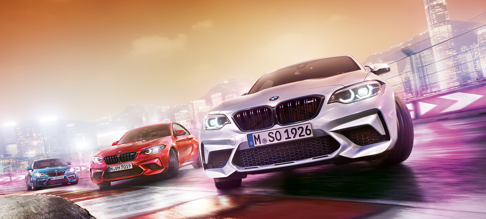 BMW M2 Competition in action Three BMW M2 Competition drifting on race track in front of nocturnal cityscape.Three BMW M2 Competition drifting on race track in front of nocturnal cityscape.
