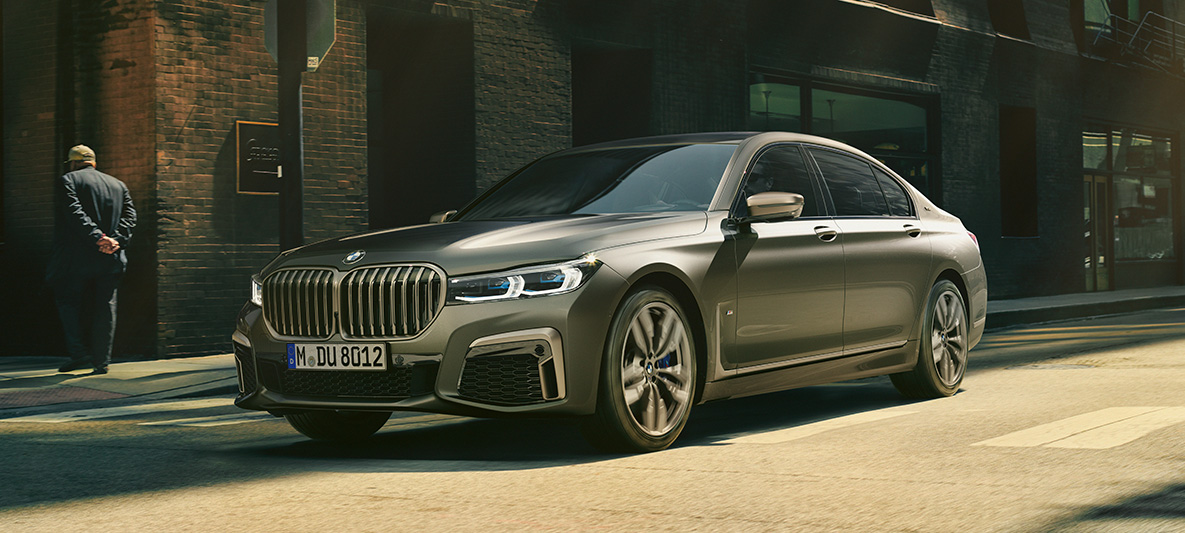 BMW M760Li xDrive Berline G11 G12 2019 Frozen Dark Silver metallic, vue de trois quarts arrière en mouvement devant un décor urbain BMW M760Li xDrive Berline G11 G12 2019 Frozen Dark Silver metallic, vue de trois quarts arrière en mouvement devant un décor urbain