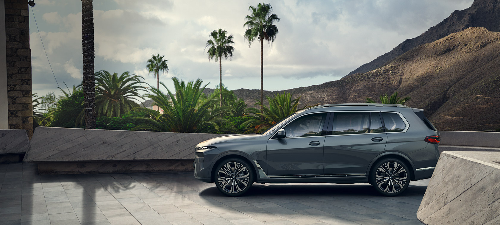 BMW X7 G07 LCI Side View Sparkling Copper Grey metallic Design Pure Excellence BMW X7 G07 LCI Side View standing in front of trees Sparkling Copper Grey metallic Design Pure Excellence