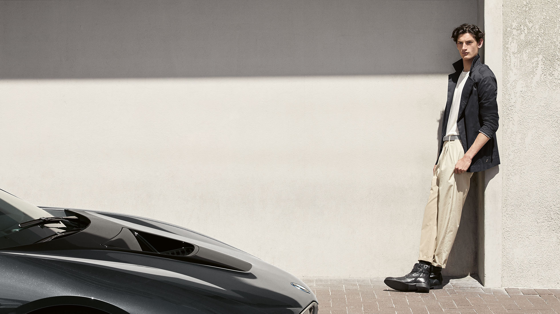 BMW i Collection. The picture shows a man leaning against a wall in a BMW i Jacket, Men from the BMW i Collection.