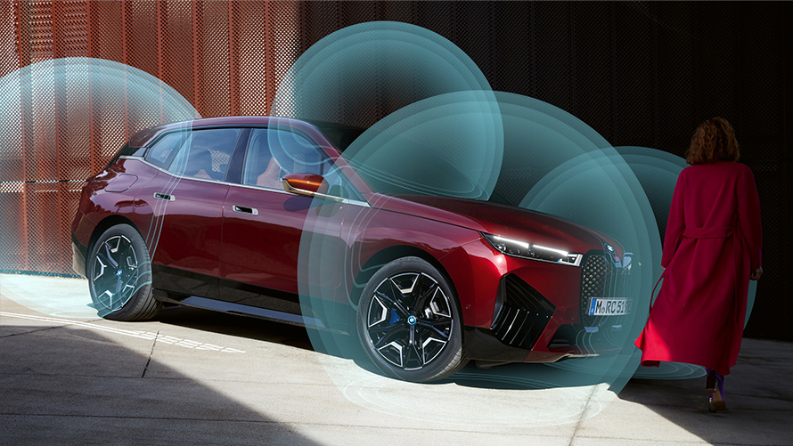 Woman in red coat in front of BMW iX (i20) BMW Digital Keys BMW Digital Keys Woman in red coat in front of BMW iX (i20) in three-quarter view with visualised location radar