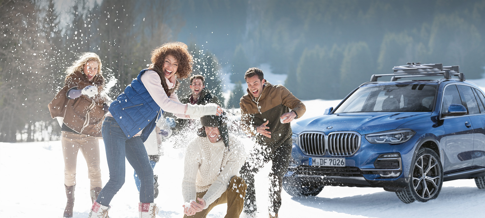 Accessoires BMW d’origine et Service BMW, automne-hiver Une femme et un homme rient dans la neige, devant une BMW