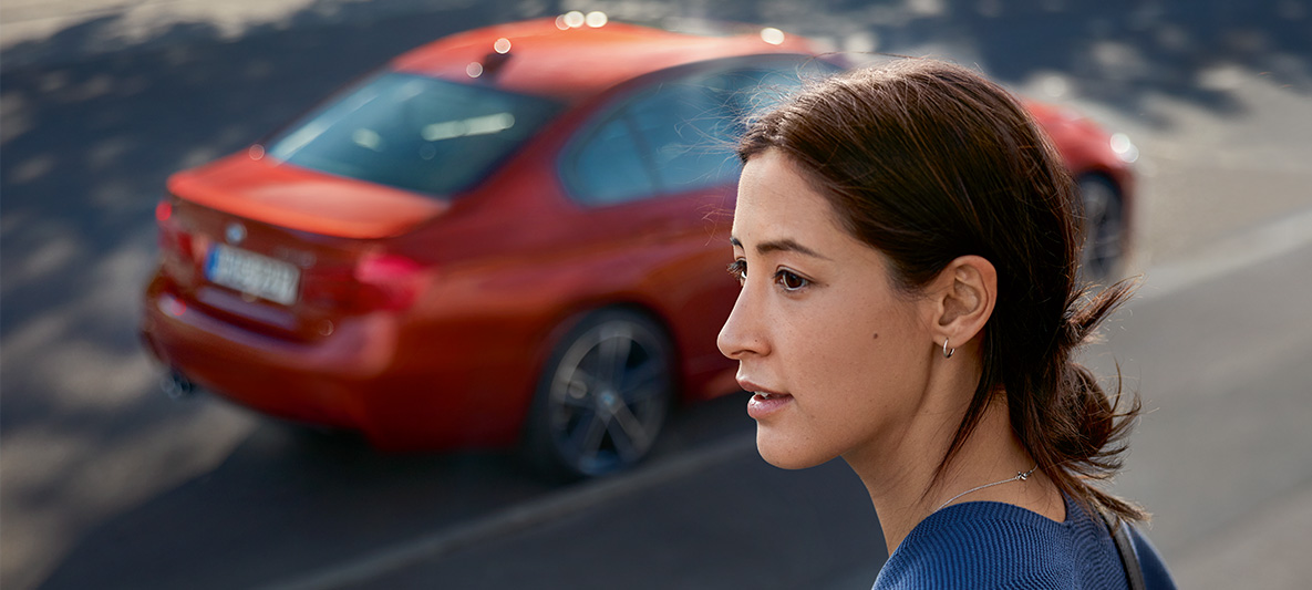 Une femme regarde au loin. Derrière elle, une BMW passe. Une femme regarde au loin. Derrière elle, une BMW passe.