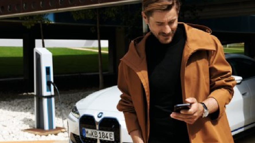 Man on phone walking away from BMW that is charging. 