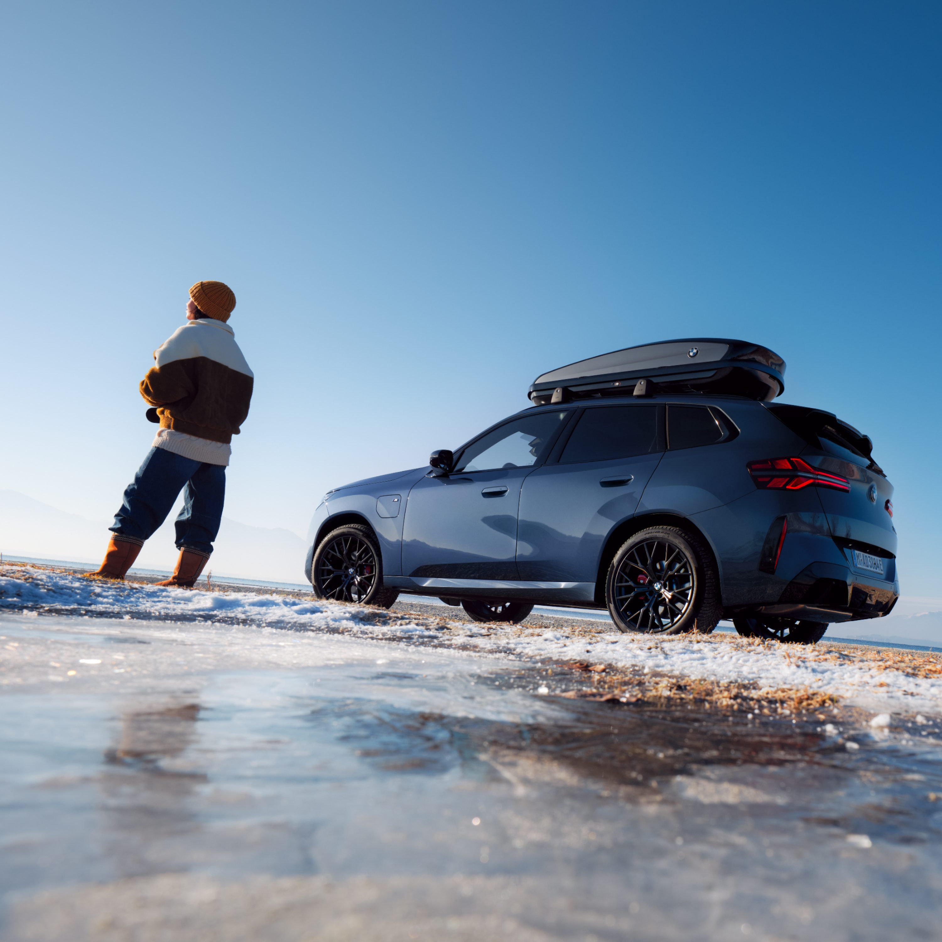 Two people standing in front of a BMW X3 with rooftop box gazing into the distance